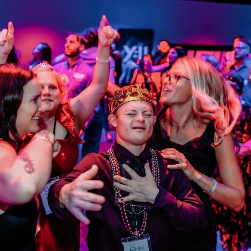 Joey wearing a king's crown on a dance floor surrounded by friends and family.